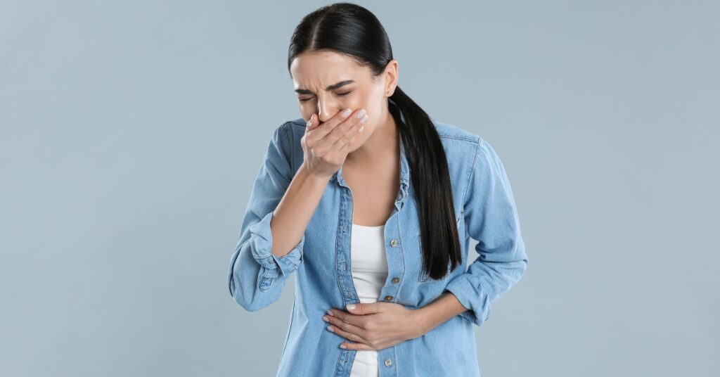 Woman covering her mouth with nausea while holding her stomach